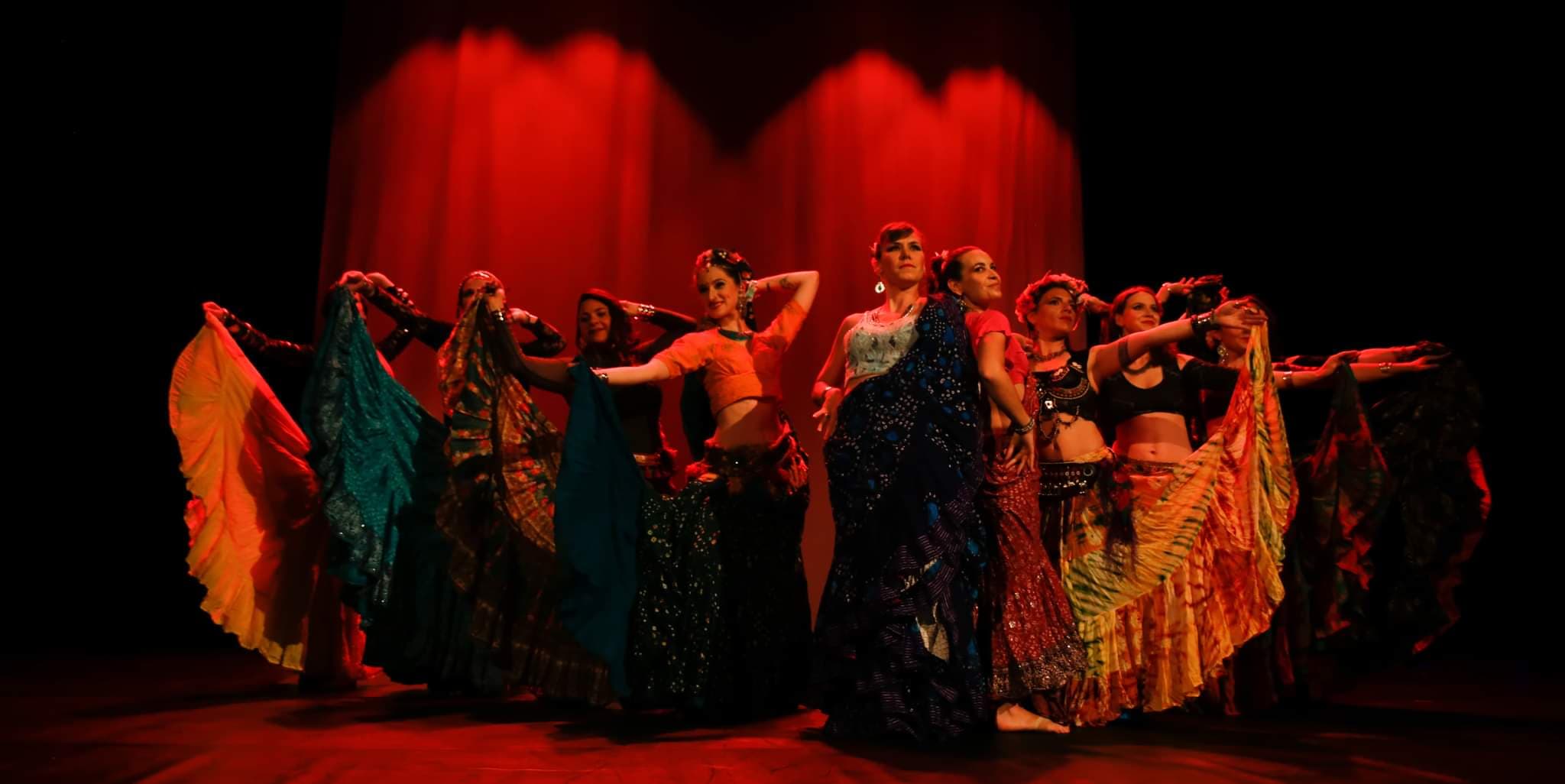Photo des danseuses ATS de la troupe Saudade sur scène positionnées en triangle en pointe, qui lèvent un pan de leurs jupes vers le public.
