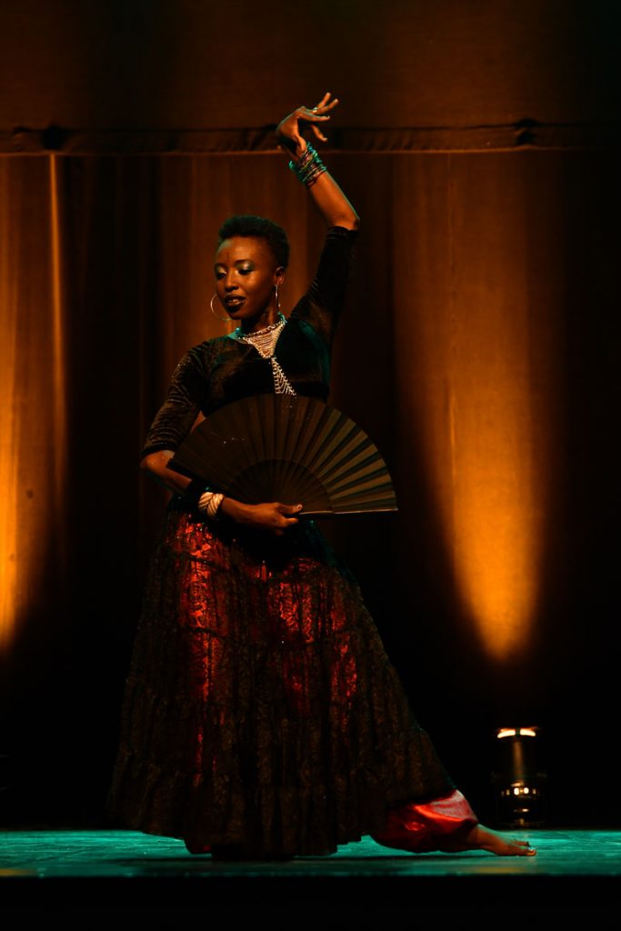photo d'Alina de la comédie tribale à Bordeaux, sur scène avec un éventail et une jupe rouge pailletée dans un univers flamenco