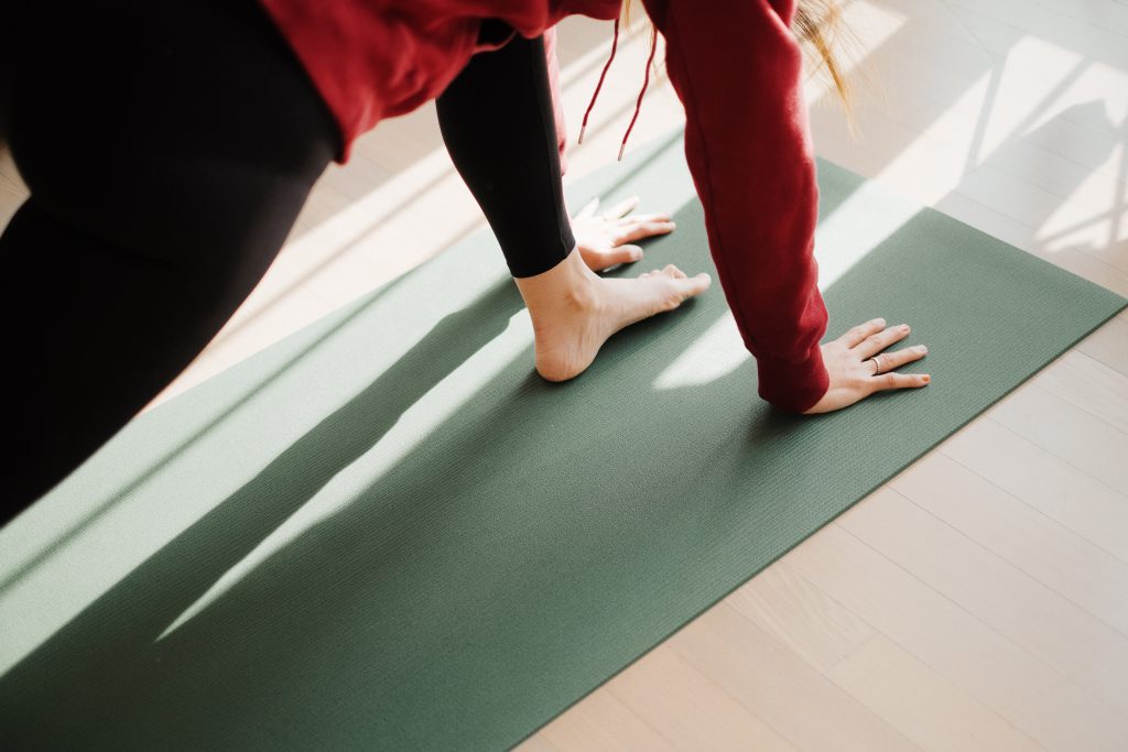 femme pratiquant le yoga sur un tapis vert pour illustrer la pratique du yoga, prise en contre plongée on ne voit que ces mains et un pied sur le tapis