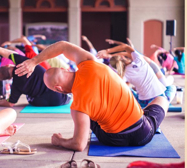 photo d'un cours collectif de yoga de dos avec au centre de la photo un homme adulte ou senior entrain de pratiquer