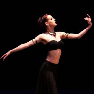 photo d'Elaïs dansant sur scène de profil avec les bras en ouverture, fond noir